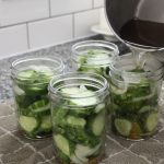 Pouring pickling liquid into pints of bread and butter pickles