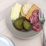 Plate of crackers, cheddar cheese, dried salami and old-fashioned bread and butter pickles with fork