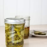 Two jars of bread and butter pickles, one opened. Plate blurred in the background