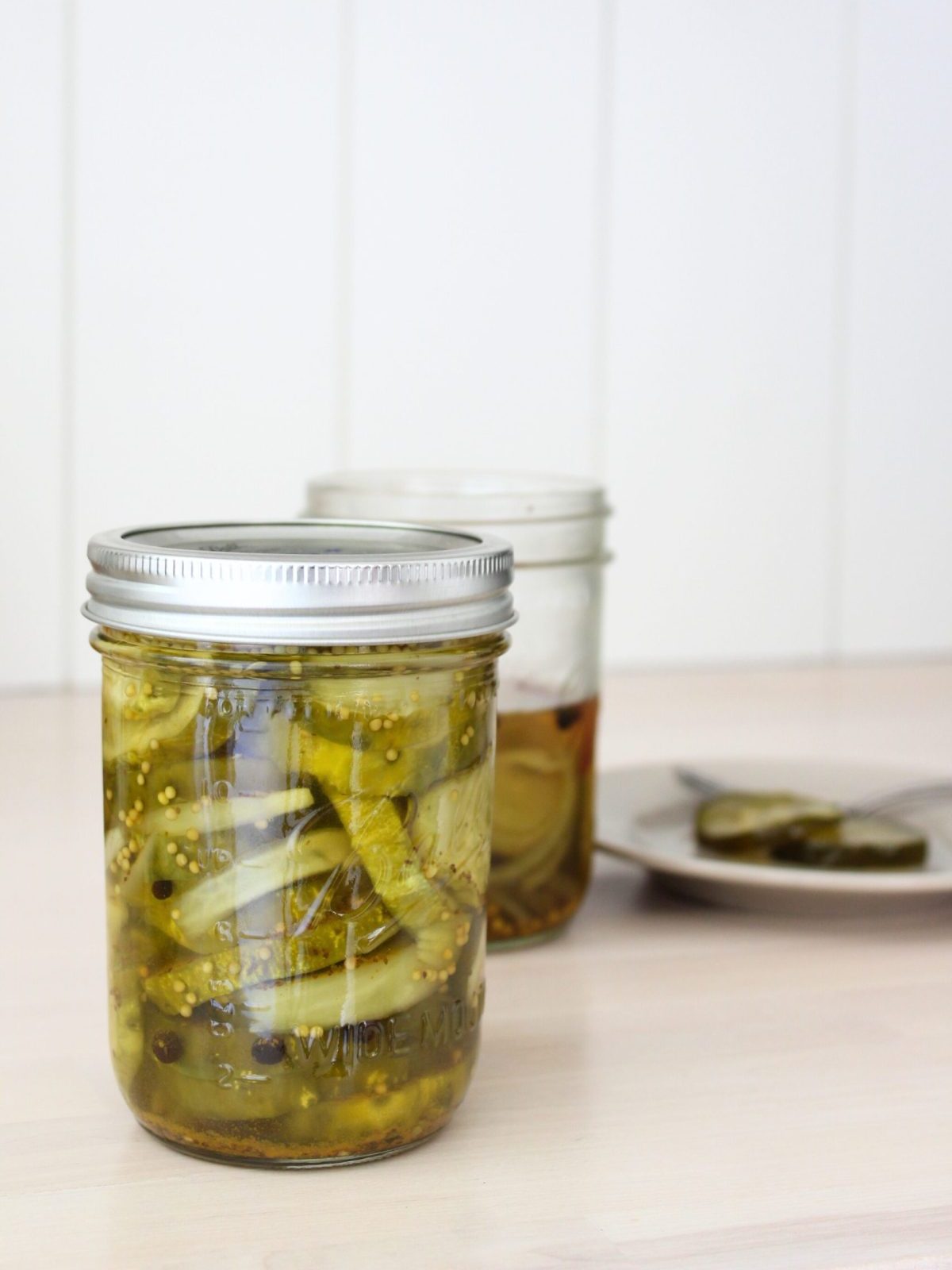 Two jars of bread and butter pickles, one opened. Plate blurred in the background