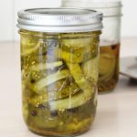 Two jars of bread and butter pickles, one opened. Plate blurred in the background