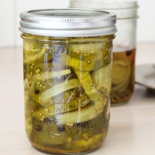 Two jars of bread and butter pickles, one opened. Plate blurred in the background
