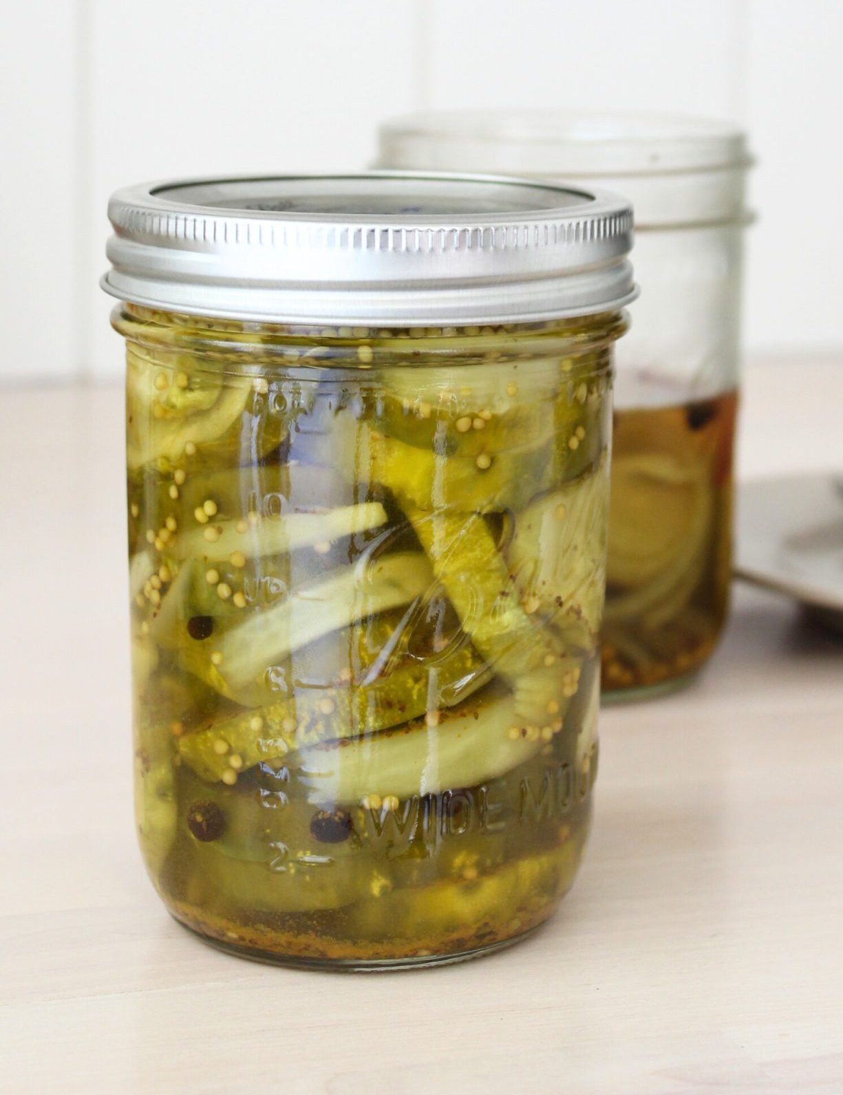 Two jars of bread and butter pickles, one opened. Plate blurred in the background