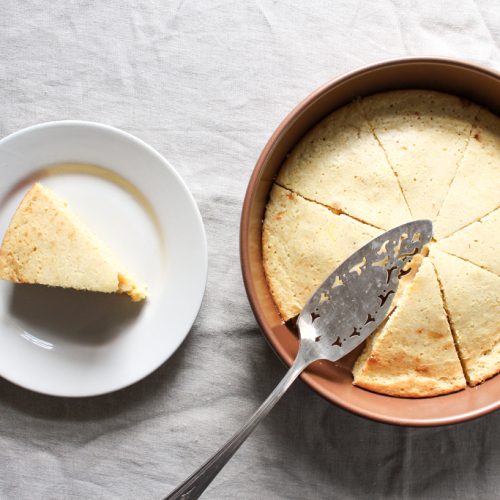 Slice of homemade cornbread and pan of from-scratch cornbread with cake knife on linen background