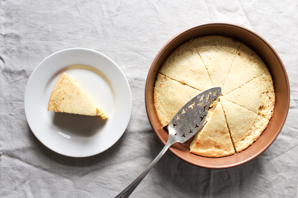 Slice of homemade cornbread and pan of from-scratch cornbread with cake knife on linen background