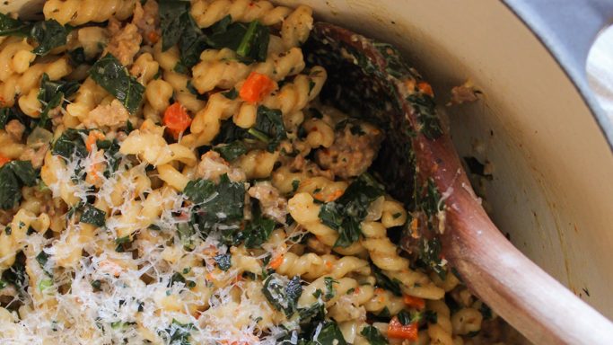 Overhead shot of One Pot Pasta with Sausage and Kale in dutch oven with wooden spoon