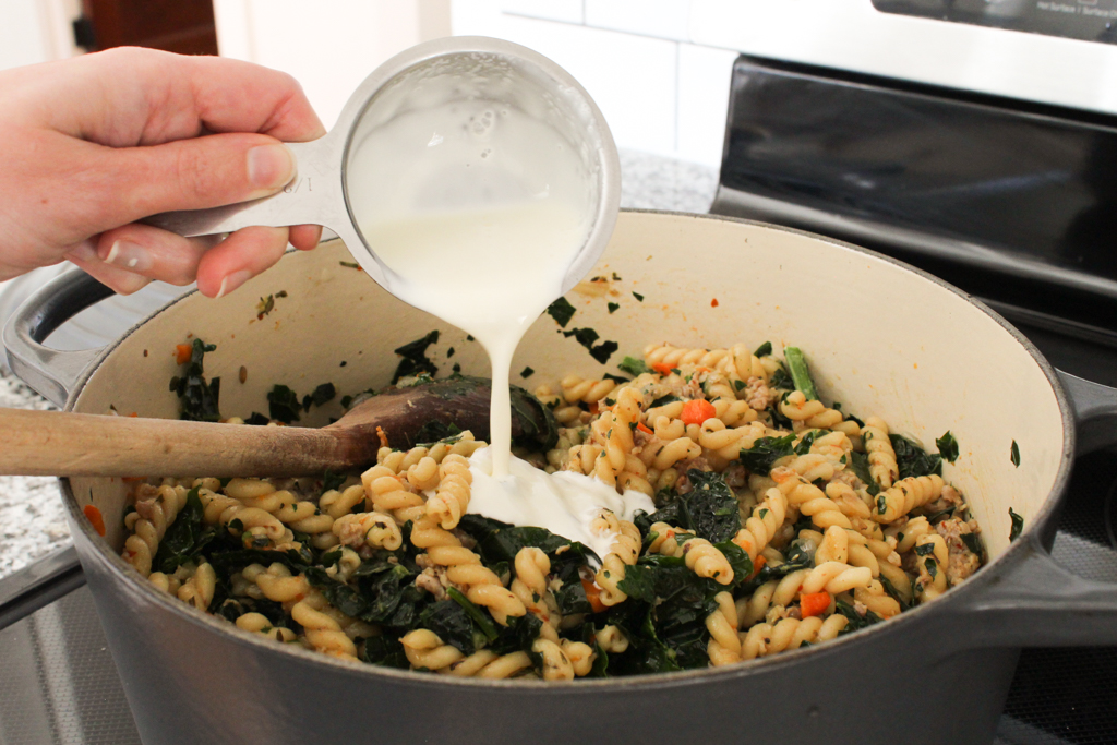 Pouring heavy cream into One Pot Pasta with Sausage and Kale recipe
