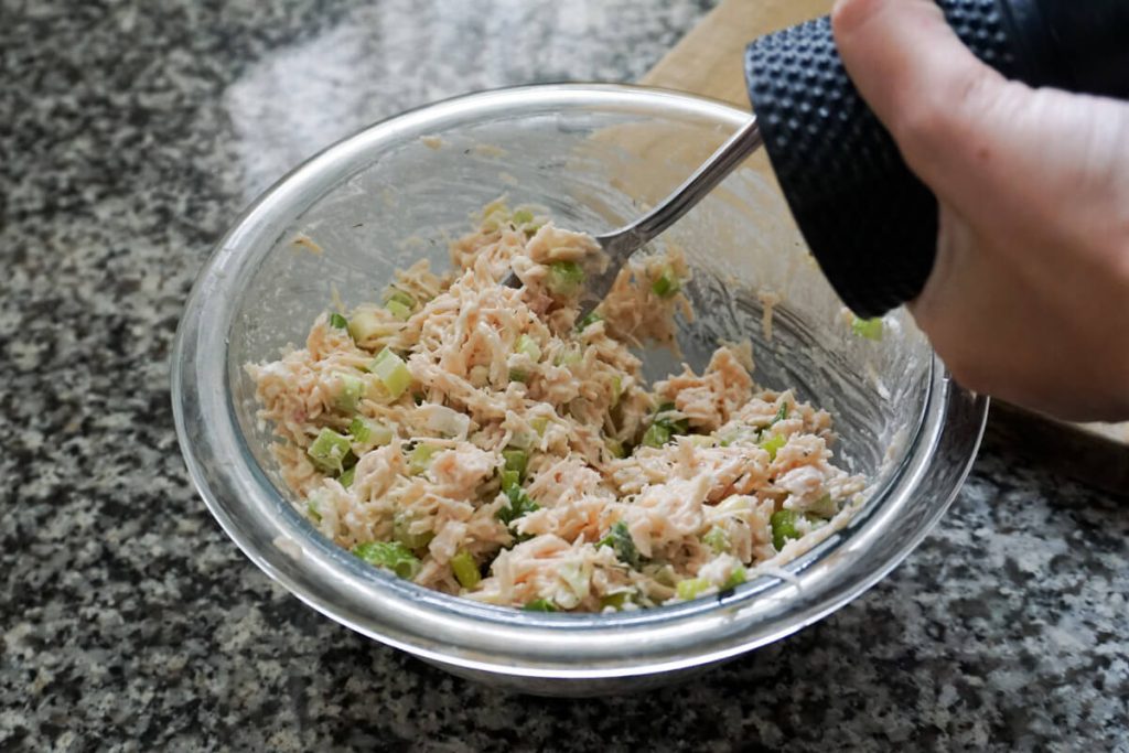 Canned chicken salad in a mixing bowl with dill and mustard, seasoning to taste