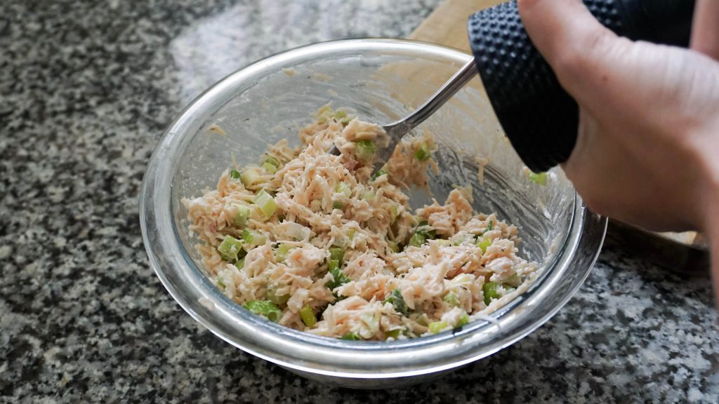 Canned chicken salad in a mixing bowl with dill and mustard, seasoning to taste