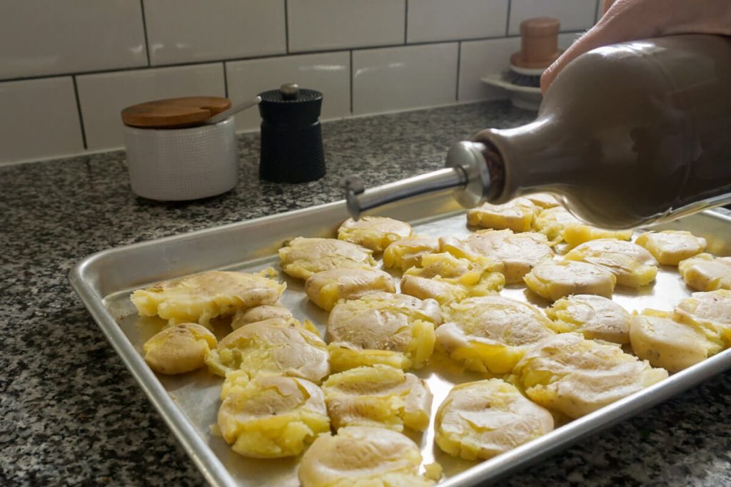 Drizzling oil over crispy smashed potatoes side dish