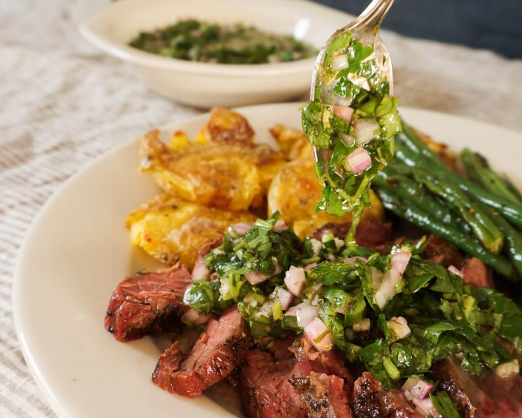 Drizzling fresh chimichurri sauce on grilled steak