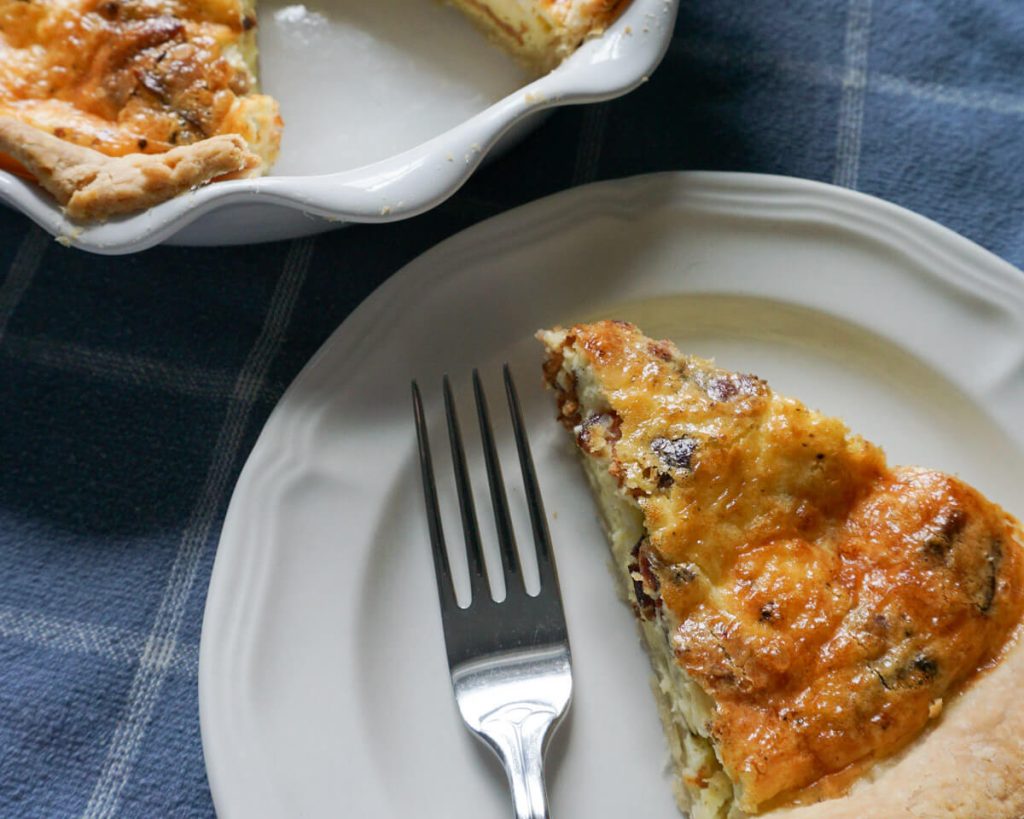 Slice of simple cheese and bacon quiche with homemade crust