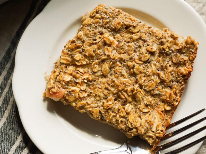 slice of apple pie baked oatmeal on plate next to prepared 9x13 dish of fall make ahead breakfast idea