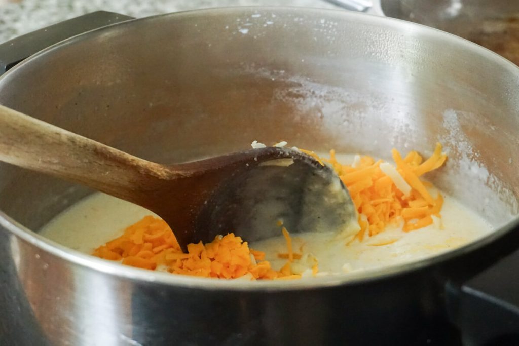 adding grated cheese to macaroni cheese sauce recipe